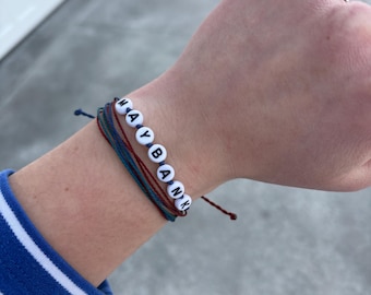 May include: A bracelet with the word "MAYBANK" spelled out in white beads on a blue, red, and green string.
