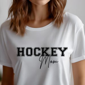 May include: White t-shirt with black text that reads "HOCKEY Mom" in a varsity style font.