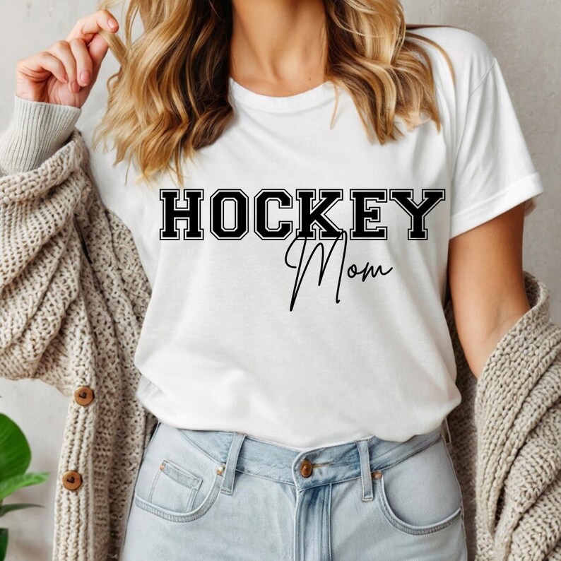 May include: White t-shirt with black text that reads "HOCKEY Mom" in a varsity style font.
