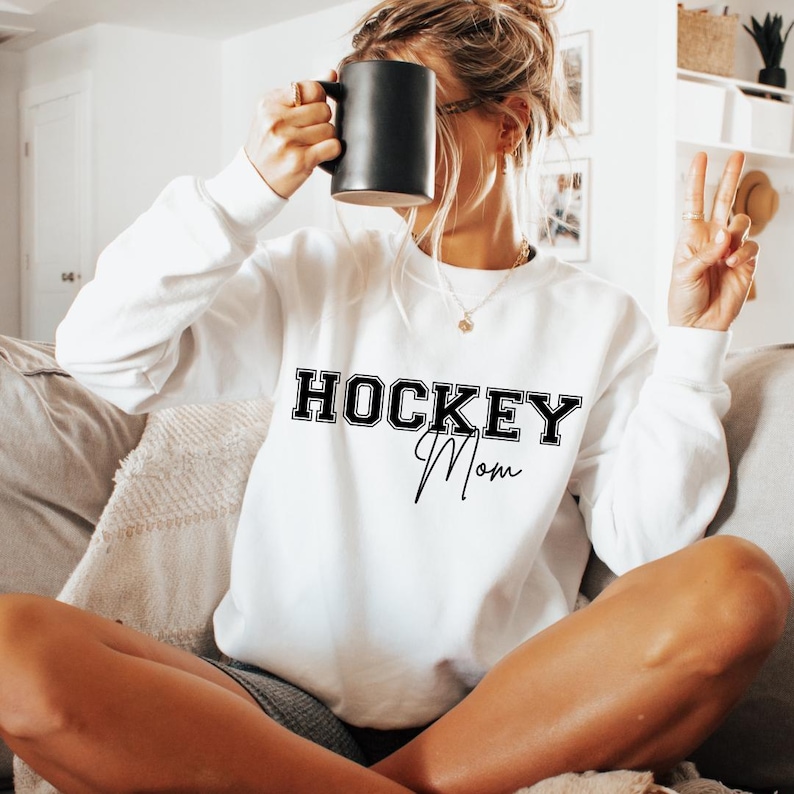 May include: White sweatshirt with black text that reads "HOCKEY Mom" in a varsity style font.