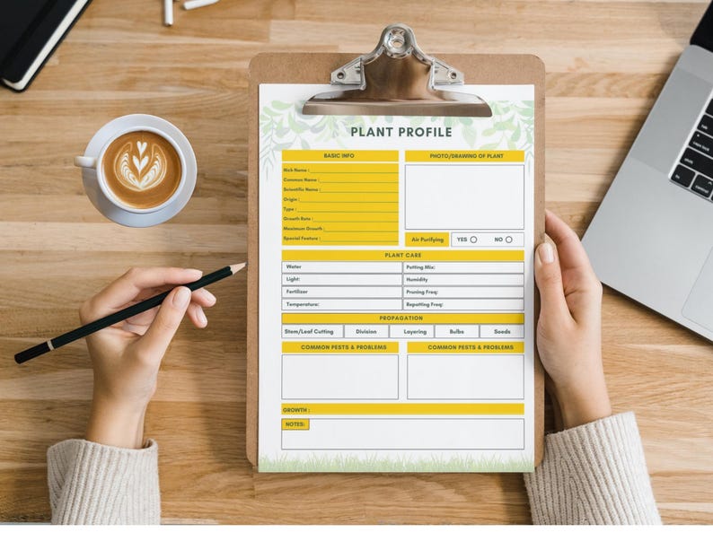 May include: A clipboard with a "PLANT PROFILE" form, held by a person. The form has sections for basic info, plant care, and propagation. A cup of coffee and a laptop are on the wooden surface. A pencil is held near the form.