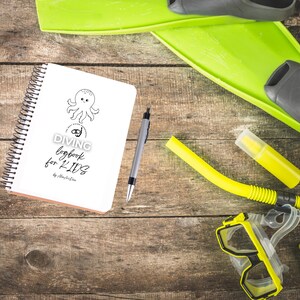 May include: A spiral-bound notebook with the text "DIVING logbook for KIDS" and an octopus illustration, alongside diving gear: yellow snorkel, mask, fins, and a pen. The items are arranged on a wooden surface.