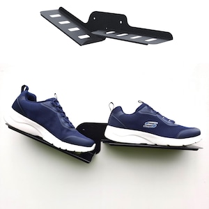 Op de afbeelding: Twee paar donkerblauwe sportschoenen met witte zolen worden getoond op een zwart metalen schoenenrek. Het rek is gemonteerd aan een witte muur.