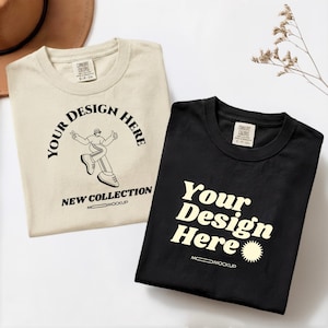 May include: Two t-shirts, one cream-colored and one black, are displayed. The cream shirt features a graphic with the text "YOUR DESIGN HERE" and "NEW COLLECTION." The black shirt has the text "Your Design Here." Both shirts have a tag that reads "COMFORT COLORS."