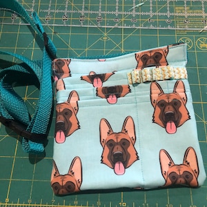 May include: A light blue fabric pouch with a German Shepherd dog print. The pouch has multiple pockets and a turquoise strap with a black buckle. The pouch has a gold trim.