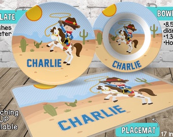 May include: Personalized cowboy themed children's dinnerware set with a 10-inch plate, 8.5-inch bowl, and a 17 x 11-inch placemat. The set features a cartoon cowboy riding a horse with the name "Charlie" on each piece. The placemat has a blue border and a free activity printed on the back.