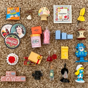 Könnte beinhalten: Eine Sammlung von Miniaturspielzeugen und Sammlerstücken, darunter ein Monopoly-Spiel, Coca-Cola-Untersetzer, eine Jolly Rancher-Süßigkeitenpackung und eine Schlumpfine-Figur. Weitere Artikel sind ein Briefkasten, ein Eisbehälter und eine Geschenkbox.