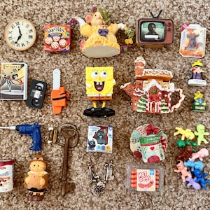 May include: A collection of miniature items including a clock, a Bagel Bites box, a yellow SpongeBob figure, a gingerbread house teapot, a blue drill, a large metal key, a Hot Dogs package, and various small plastic figurines and accessories.