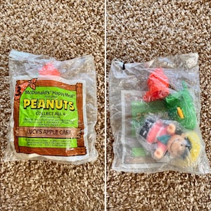 May include: Two sealed McDonald's Happy Meal toys featuring Peanuts characters. One package displays the text "LUCY'S APPLE CART" and "COLLECT ALL 4". The other package contains a Lucy figure, a green item, and a red item.