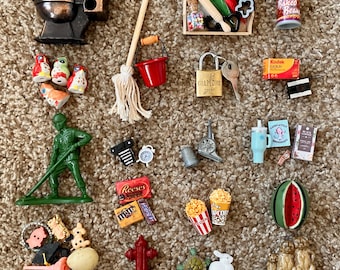May include: A collection of miniature toys and trinkets, including a toilet, a soldier, a padlock, a can of beans, and a watermelon slice. Other items include a broom, a bucket, and miniature food items.