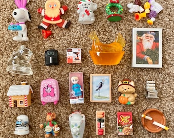 May include: A collection of miniature figurines and objects, including a Snoopy figure, Santa Claus, a dog, a wreath, a picture of Santa Claus, a doll, a house, a suitcase, a mouse, a vase, and a bowl.