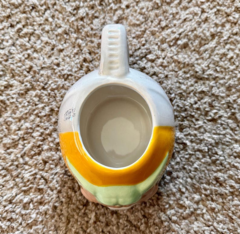 May include: A ceramic mug with a rounded body and a handle. The mug features a design with white, yellow, and green colors. The mug is designed to hold beverages.