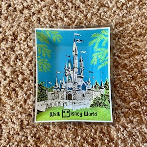 May include: A vintage glass ashtray with a blue background featuring a colorful illustration of Cinderella's castle at Walt Disney World. The text "Walt Disney World" is printed below the image.