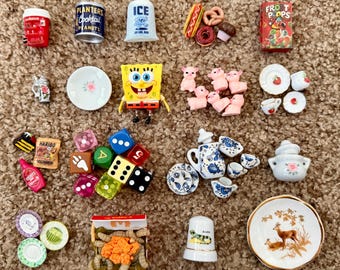 May include: A collection of miniature toys and figurines, including a red soda cup, a can of peanuts, a bag of ice, a box of cereal, and a SpongeBob SquarePants figure. Also includes dice, plates, and a thimble.