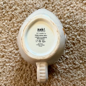 May include: A white ceramic mug with a handle, featuring the brand name "zak!" and the text "HAND WASH ONLY". The bottom of the mug also includes the text "&copy; & &trade; Lucasfilm Ltd." and "04/2022 CHINA CHINE 19343".
