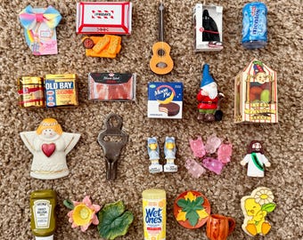 May include: A collection of miniature novelty items, including a guitar, a gnome, a bottle of Mentos, and a miniature box of Moon Pie chocolate cakes. Other items include a miniature angel figurine and a bottle of Heinz Sweet Relish.