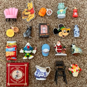 Könnte beinhalten: Eine Sammlung von Miniaturfiguren und Objekten, darunter ein rosa Sessel, Winnie Puuh, ein Hund, eine Cobra Kai-Figur, Mickey Mouse, eine Weihnachtsmannfigur, eine blaue Baseballkappe, ein Mutter-Gans-Buch und ein Blumenarrangement.