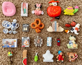 May include: A collection of miniature toys and decorative items, including a pink chair, a mermaid doll, a Minnie Mouse figurine, a jack-o'-lantern, a turtle, a pretzel, a tea set, a BB-8 figure, and a koala with a candy cane.
