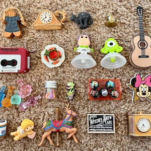 May include: A collection of miniature decorative items, including a red cassette tape, a guitar, a clock, and various character figurines. The items are arranged on a brown carpet.