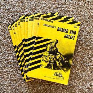Może przedstawiać: Stos żółtych książek Cliffs Notes o Romeo i Julii Szekspira. Książki mają czarno-żółte ukośne paski i zawierają ilustrację postaci z dramatu. Widoczny jest również tekst "Cliffs Notes" i "Your Key to the Classics".