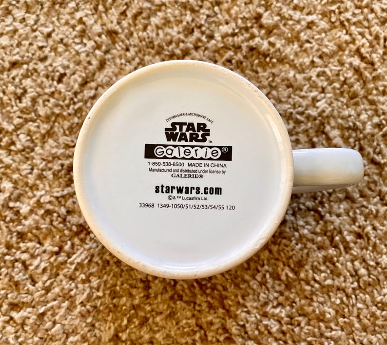 May include: A white ceramic mug with a handle, featuring the Star Wars logo and the Galerie brand. The bottom of the mug displays text including "Dishwasher & Microwave Safe" and "Made in China."