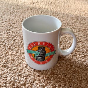以下が含まれることがあります： 白いセラミックコーヒーマグ、湾曲したハンドル付き。マグには「Espresso Roast」の文字とピサの斜塔の描写が描かれたカラフルなグラフィックが特徴です。スターバックスコーヒーのロゴも表示されています。