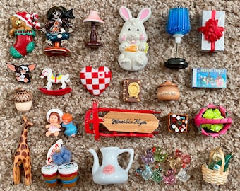 May include: A collection of miniature figurines and ornaments, including a bear in a Christmas stocking, a scarecrow, a bunny holding a carrot, a blue lamp, a gift box with a red bow, a Gremlin, a rocking horse, a heart, a book, a cookie jar, a sled, a basket, and a giraffe.