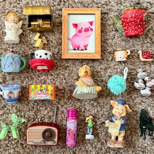 May include: A collection of miniature figurines and objects, including a framed pig painting, a strawberry teapot, a radio, a treasure chest, and a box of Otter Pops. Other items include a teacup, a sponge, and a balloon dog.