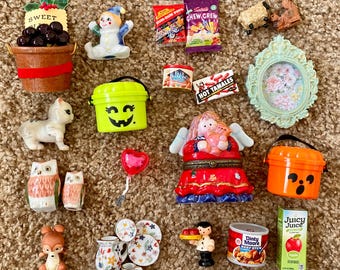 May include: A collection of miniature figurines and food items, including a pumpkin bucket, a clown, a cat, owls, a deer, and a heart-shaped balloon. There are also small food packages, a decorative frame, and a juice box.