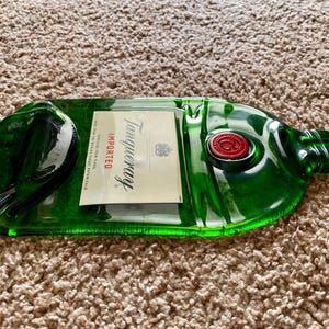 May include: A green glass bottle shaped like a Tanqueray gin bottle. The bottle is empty and has a red wax seal on the top. The label reads "Tanqueray Imported".