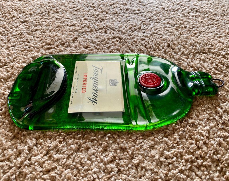 May include: A green glass bottle shaped like a Tanqueray gin bottle. The bottle is empty and has a red wax seal on the top. The label reads "Tanqueray Imported".