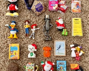 Puede incluir: Una colección de figuras en miniatura y artículos novedosos, que incluyen una figura de Mickey Mouse, una figura de Pato Donald y una figura de Papá Noel. Otros artículos incluyen una caja de Uncrustables, una caja de cereales Golden Crisp y una pintura en miniatura enmarcada.