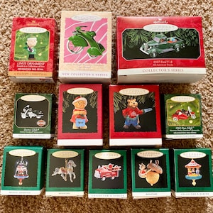 May include: A collection of Hallmark Keepsake Christmas ornaments in their original boxes. The boxes are red, green, and black, featuring images of vehicles, characters, and scenes. The ornaments include a Snoopy Christmas, a motorcycle, and a fire truck.