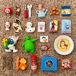 May include: A collection of miniature items including a red number 11 ball, a witch pin, a screwdriver, a wrench, a rabbit with a watering can, a teddy bear, Crayola crayons, a Hello Kitty figure, a snowman, a duck, a Tamagotchi, a Spider-Man figure, a penguin, a Smurf, Oogie Boogie, a Donald Duck notepad, a turtle, a Belle plate, three keys, bread, red pepper flakes, a blue Vulcan tape measure, and a box of Bagel Bites.