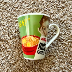May include: A ceramic mug with a green background featuring a Kellogg's Rice Krispies cereal bowl illustration and the words "RICE KRISPIES". The mug has a white handle and a vintage-style image of a person.