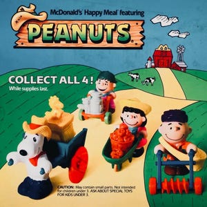 May include: McDonald's Happy Meal toys featuring Peanuts characters. The image shows four figurines: Snoopy with a wagon, Linus with a cart, Lucy with a wheelbarrow, and Charlie Brown with a lawn roller. The text reads "Collect All 4!"