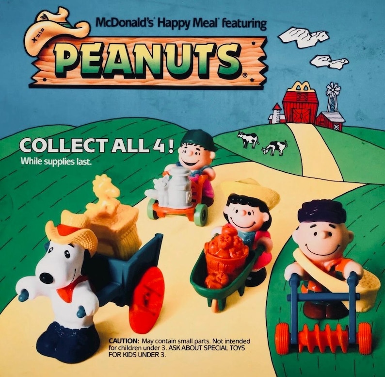 May include: McDonald's Happy Meal toys featuring Peanuts characters. The image shows four figurines: Snoopy with a wagon, Linus with a cart, Lucy with a wheelbarrow, and Charlie Brown with a lawn roller. The text reads "Collect All 4!"