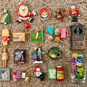 Puede incluir: Una colección de juguetes y figuras en miniatura, que incluyen un Papá Noel, una ardilla, un armario en miniatura, un vaso con temática de rana y una caja en miniatura de queso Velveeta. Otros artículos incluyen un árbol de Navidad, una muñeca y una muñeca Annabelle en miniatura.