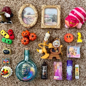 May include: A collection of miniature items including a raisin figure, two framed landscape pictures, a pink striped cat, toy cars, orange pumpkins, a television, a bottle with a portrait, a candelabra, a clock, a doll, and various small accessories.