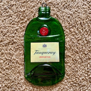 Op de afbeelding: Een groene glazen fles in de vorm van een gin-fles met een rode dop. De fles heeft een etiket met de tekst "Tanqueray Imported" en "Distilled Four Times. Made from the World's Finest Botanicals."