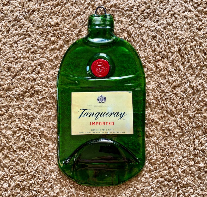 May include: A green glass bottle shaped like a gin bottle with a red cap. The bottle has a label that says "Tanqueray Imported" and "Distilled Four Times. Made from the World's Finest Botanicals."