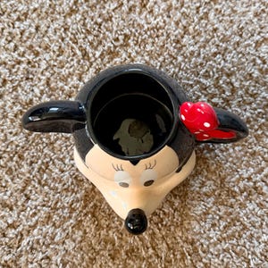 May include: A white ceramic mug with a black handle and the text "But First, Coffee" in a bold, black font. The mug is on a white surface.