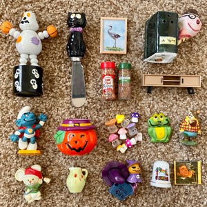 Puede incluir: Una colección de figuritas en miniatura y objetos decorativos, que incluyen un fantasma, un cuchillo de gato negro, un Pitufo, una calabaza, una rana y un ratón. También hay pequeños frascos de especias, una pintura en miniatura y un pequeño mueble de TV.