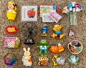Puede incluir: Una colección de artículos novedosos coloridos, que incluyen figuras de una vaca, un Pitufo y una rana, junto con un ventilador en miniatura, un frasco de vidrio con decoraciones de hongos y una variedad de otros objetos decorativos pequeños.