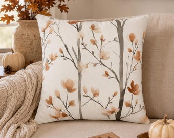 May include: A square throw pillow featuring a cream-colored fabric base with a watercolor-style print of slender dark gray tree trunks and delicate orange-brown floral blossoms scattered across the surface in a repeating botanical pattern.