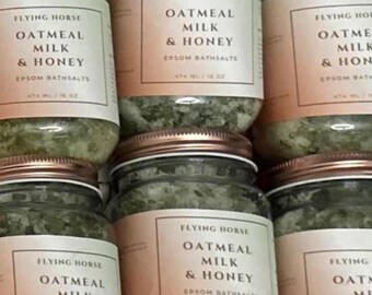 May include: Multiple glass jars filled with green bath salts. The jars have a copper lid and a white label with the text "Flying Horse Oatmeal Milk & Honey Epsom Bathsalts 473 mL / 16 oz".
