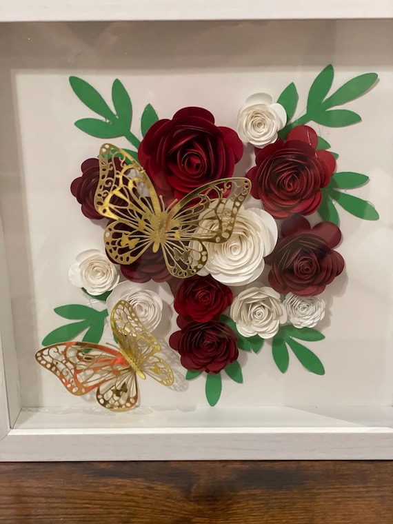 White shadow box featuring handcrafted paper flowers and delicate butterflies.