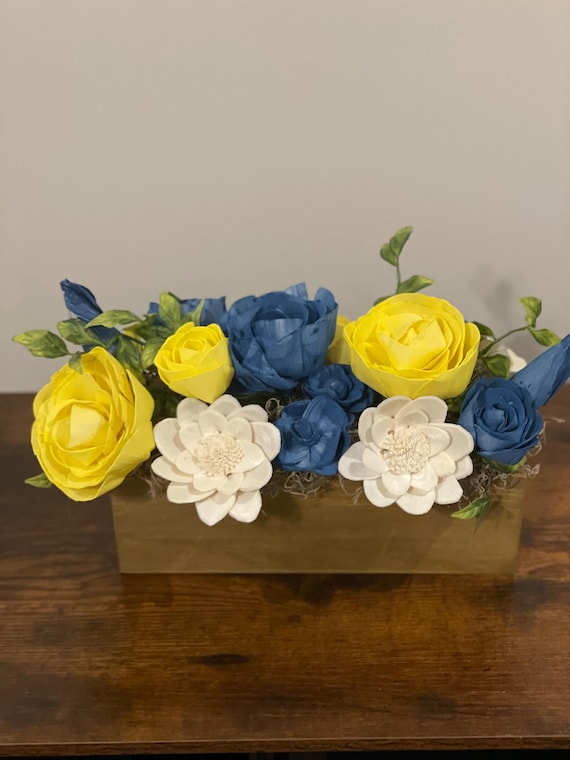 Hand-painted blue and yellow sola wood flowers beautifully arranged in a brown wooden container. A perfect addition to any room!