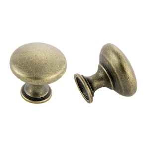 May include: Two antique brass cabinet knobs with a round top and a short, cylindrical base. The knobs have a distressed finish.