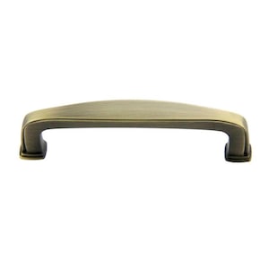 May include: A brushed antique brass cabinet pull with a slightly curved rectangular shape and squared ends.